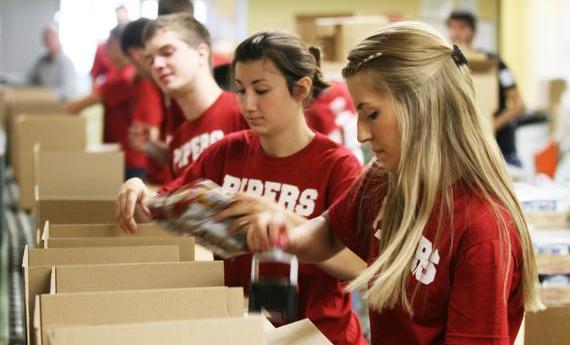 Three  student wearing red "PIPERS" shirts taping cardboard boxes while volunteering
