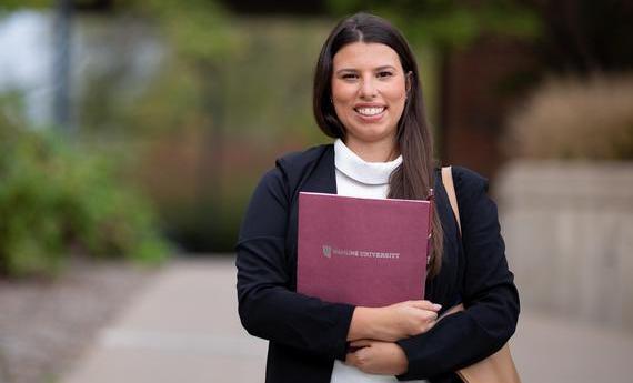 An MBA graduate student from 's School of Business holding a folder and smiling at the camera