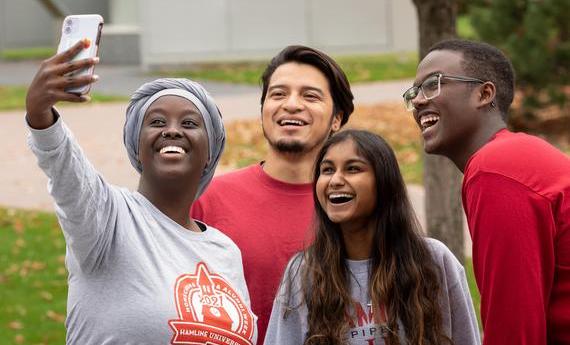 A group of four first-year  students smiling and taking a selfie on campus