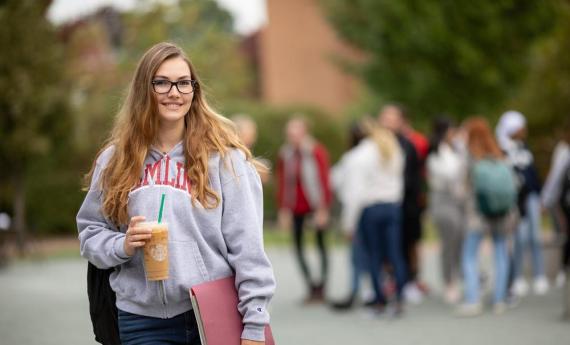 A new  student smiling outside and other students in the background