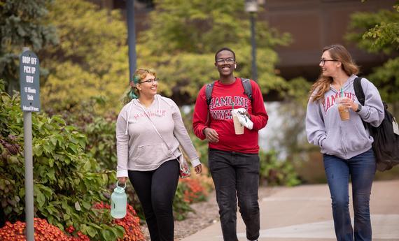 Three  students walking and talking outside on campus in the fall