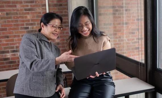 A  student and her advisor looking at a laptop together and smiling