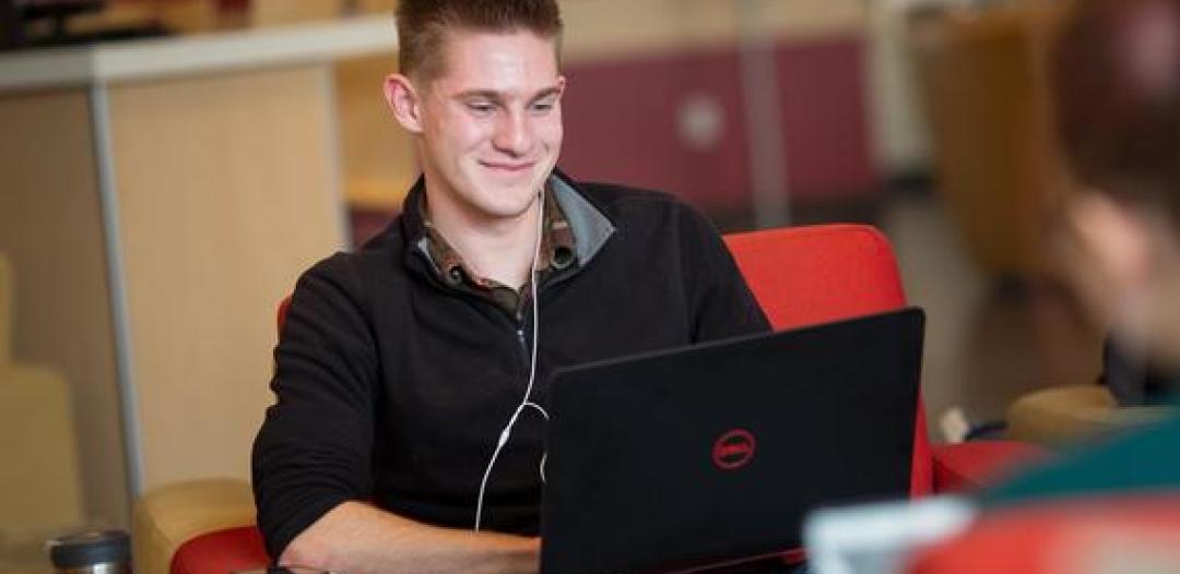 A  student sitting with a laptop on their lap, smiling and typing